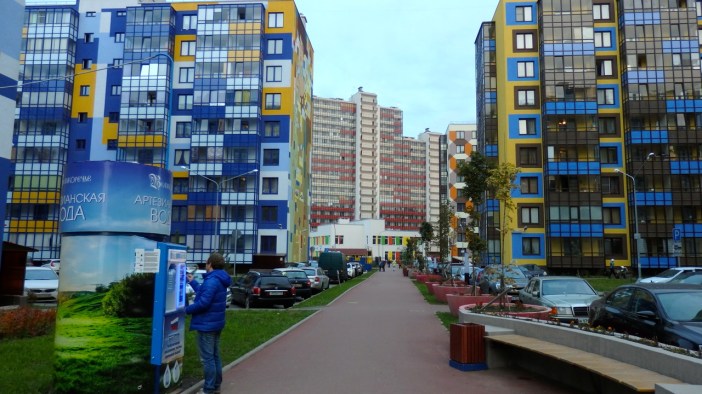 A resident purchases fresh artesian well water amidst a splashy block in New Kudrovo.